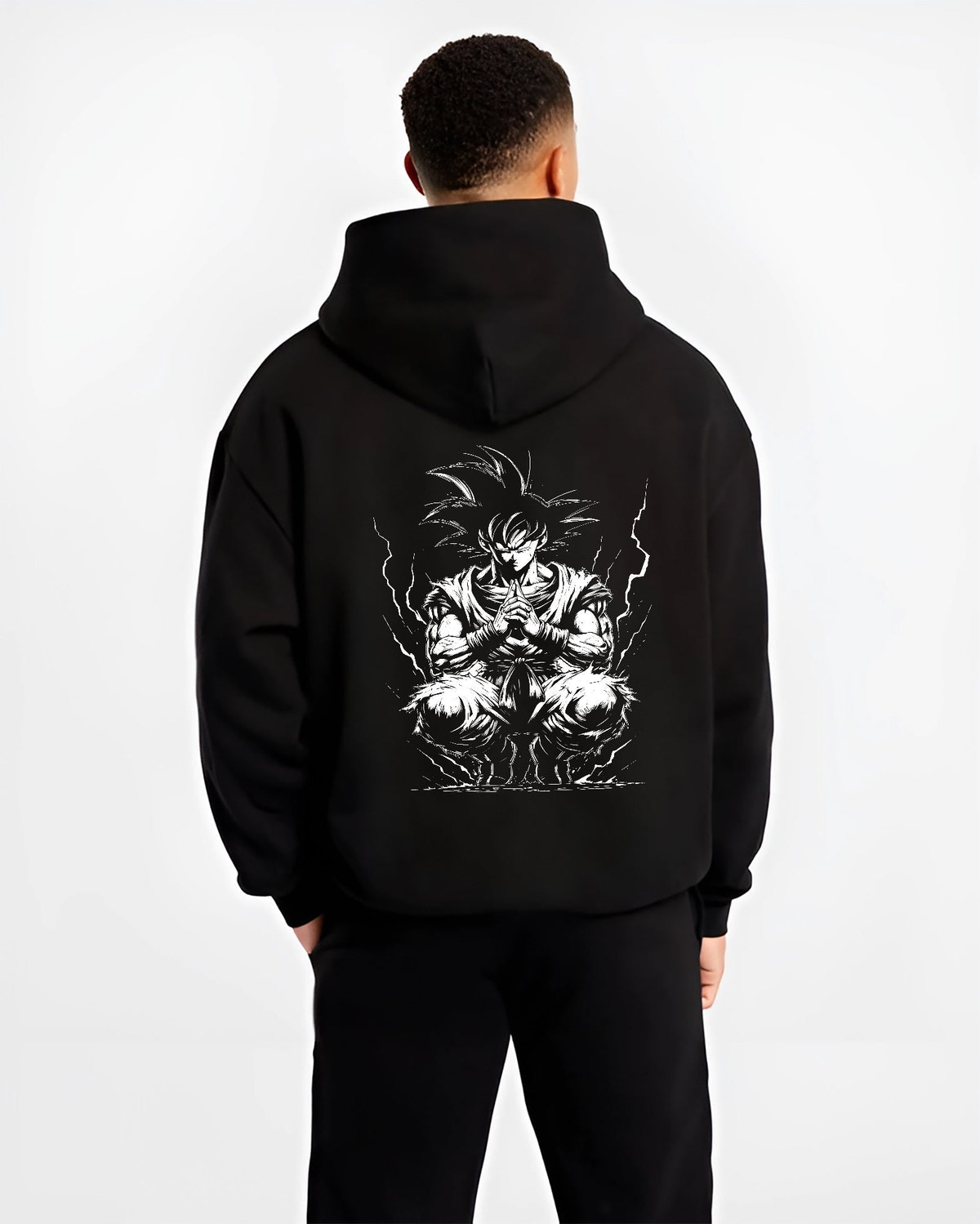 Black hoodie worn by a male model, back view, featuring Dragon Ball Goku retro manga graphic in meditation pose with glowing aura in anime poster inspired style.