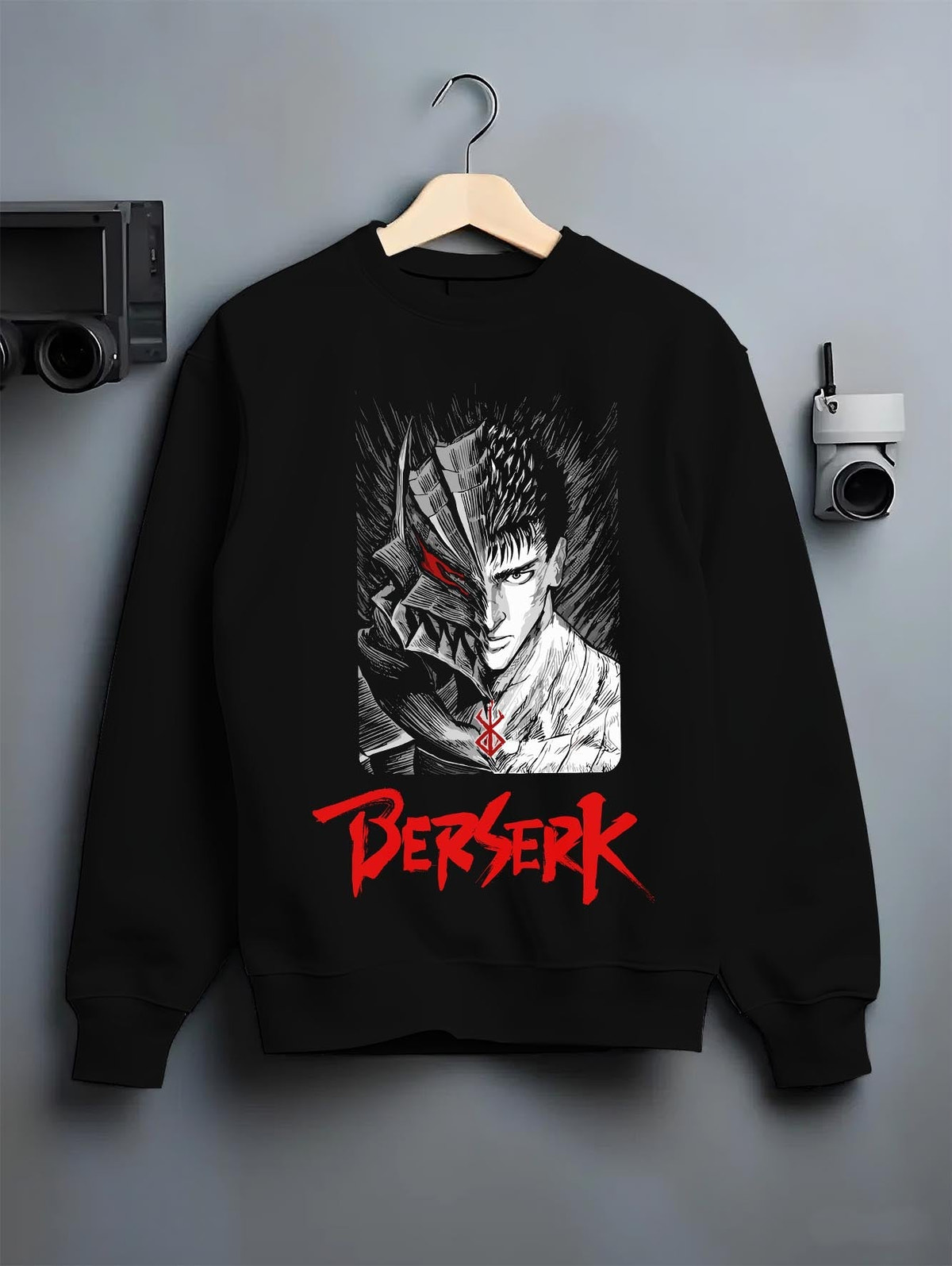 Black crewneck sweatshirt on a hanger against a grey wall, featuring Berserk Guts split armor face artwork in anime poster inspired dark manga panel design.