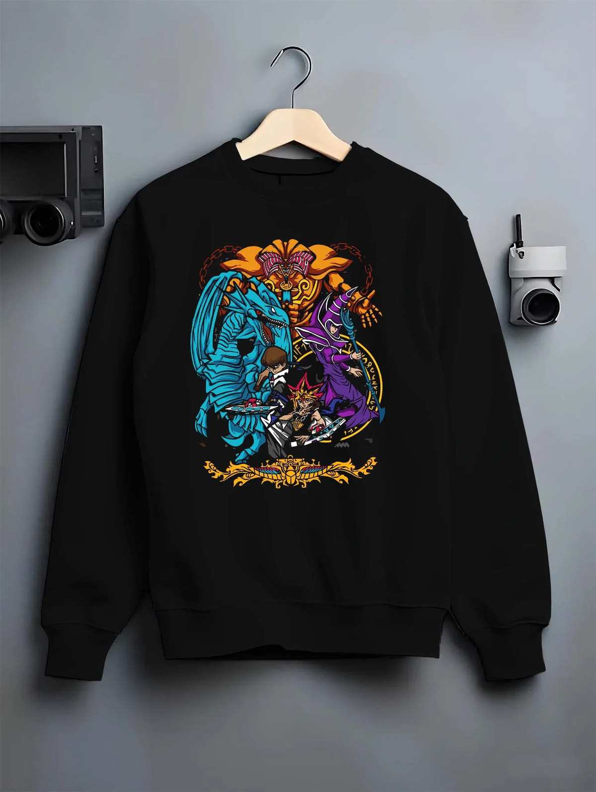 Black crewneck sweatshirt on hanger featuring Yu-Gi-Oh Egyptian Gods trio artwork.