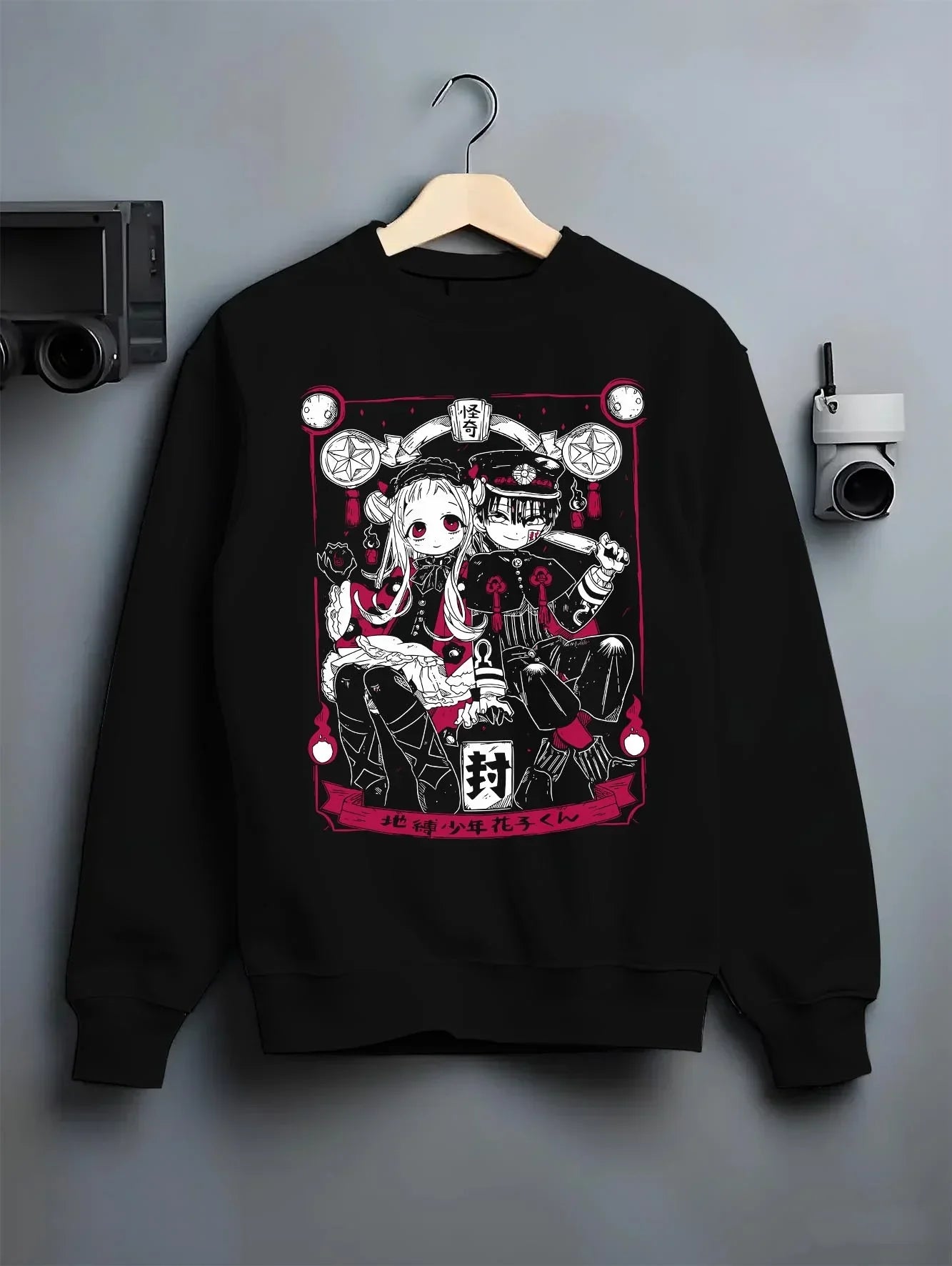 Black crewneck sweatshirt on hanger against grey wall, featuring cult classic anime poster inspired Hanako-kun and Nene Yashiro retro streetwear graphic.