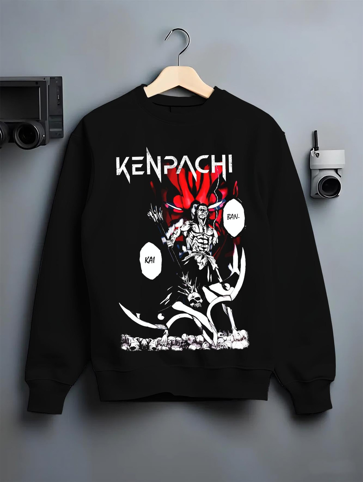 Black crewneck sweatshirt on a hanger against a grey wall, featuring Bleach Kenpachi Bankai retro streetwear graphic with bold manga panel and skull battlefield theme.