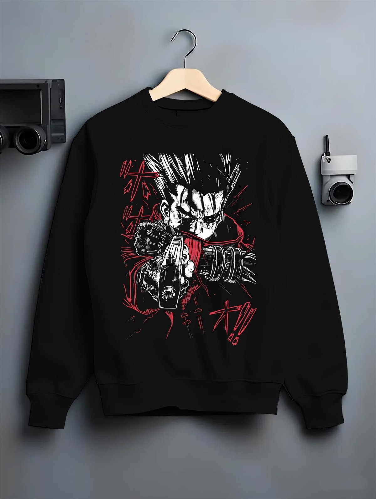 Black crewneck sweatshirt on a hanger against a grey wall, featuring Vash the Stampede dark manga panel design with retro anime-inspired weapon artwork.
