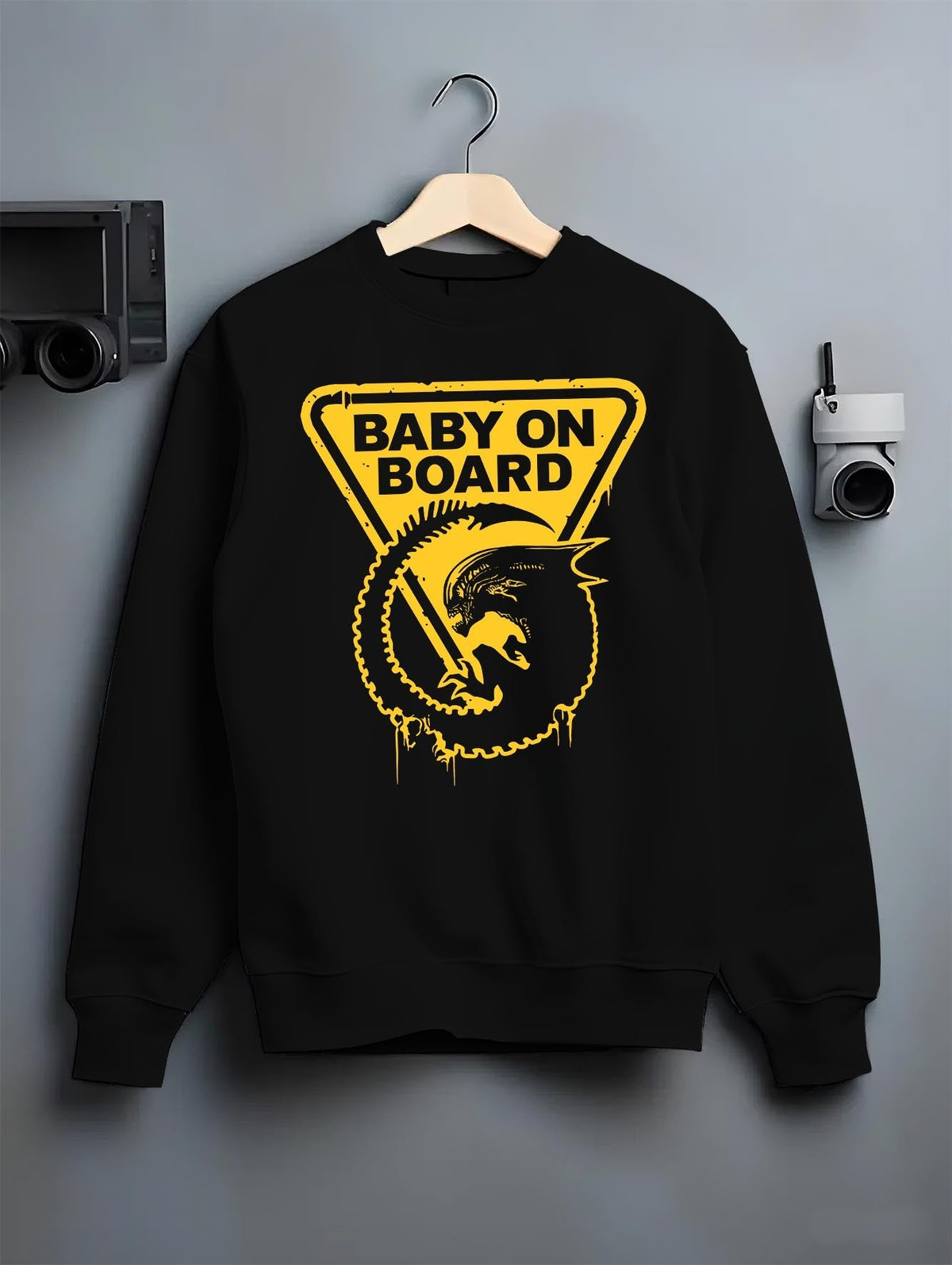 Black crewneck sweatshirt on hanger against grey wall, Alien baby on board retro sci-fi back graphic with triangle sign and drips.