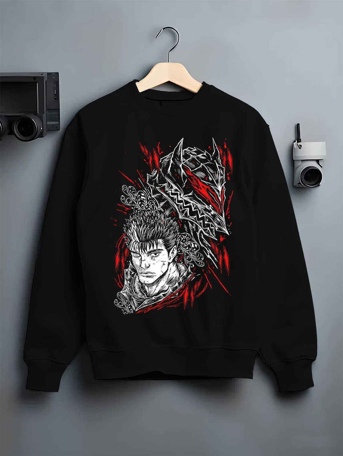 Black crewneck sweatshirt on a hanger against a grey wall, featuring Guts Berserk anime poster inspired design with manga panel graphic in striking red accents.