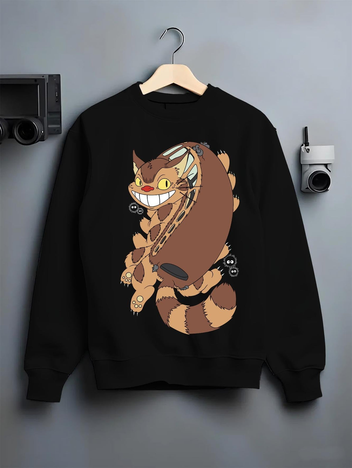 Black crewneck sweatshirt on a hanger against a grey wall, featuring Totoro Catbus and soot sprites; nostalgic 90s Japanese animation streetwear.