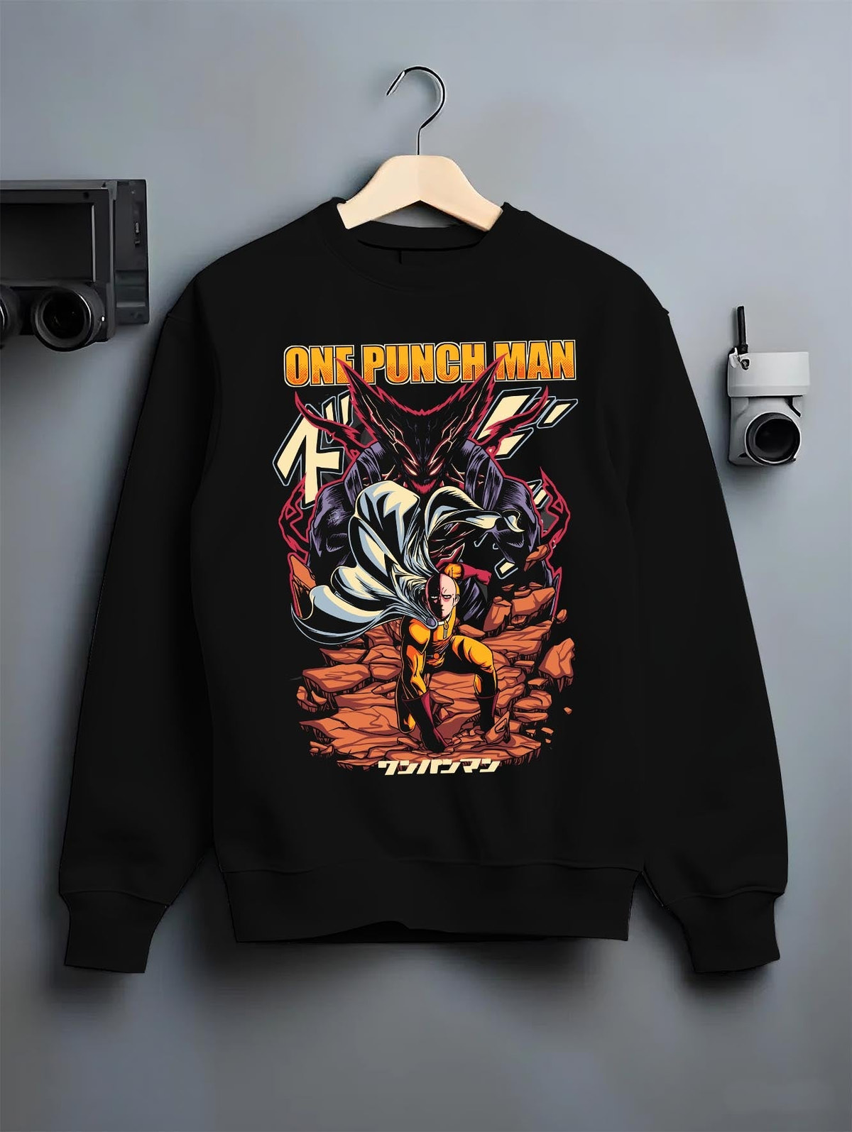 Black crewneck sweatshirt on a hanger against a grey wall, featuring One Punch Man retro streetwear graphic with dramatic battle scene of Saitama and Garou.