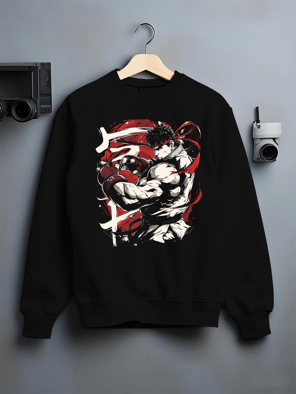 Black crewneck sweatshirt on a hanger against a grey wall, featuring Ryu Street Fighter retro streetwear graphic with iconic fighter pose and vivid red accen
