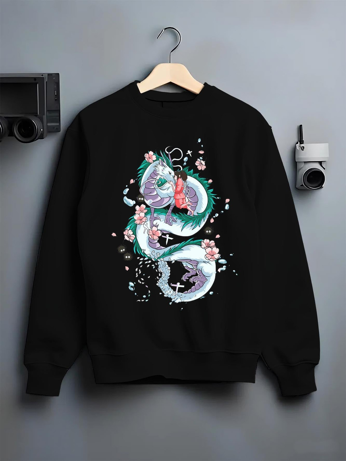 Black crewneck sweatshirt on hanger against grey wall, Spirited Away Haku and Chihiro back graphic with cherry blossom accents.