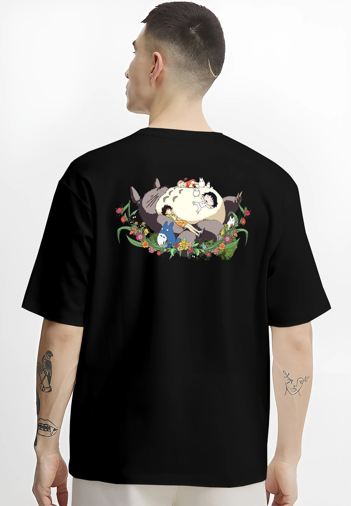 Black T-shirt worn by a male model, back view, featuring Totoro sleeping scene, urban fashion back design with nostalgic 90s floral graphic.