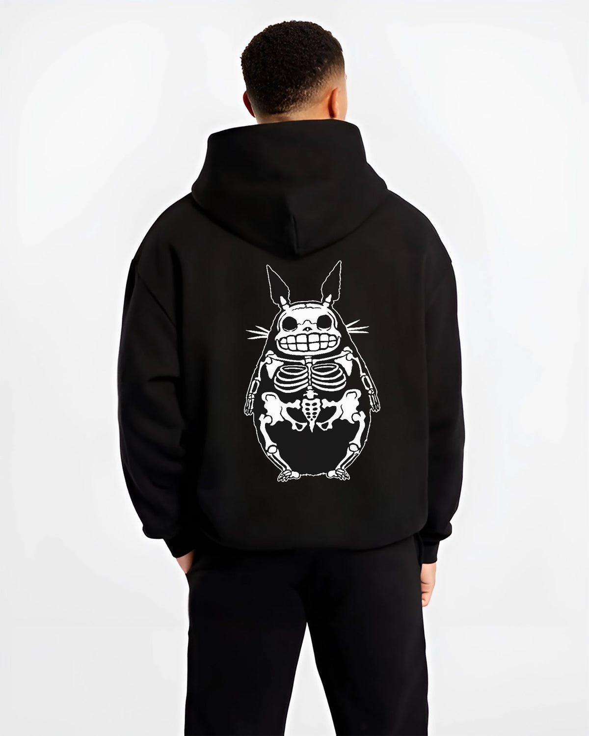 Black hoodie worn by a male model, back view, featuring Totoro skeleton x-ray artwork, retro manga graphic with bold monochrome urban fashion vibe.